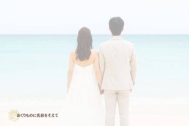 海辺で手を取り合う新郎新婦の後ろ姿。結婚祝い・名入れギフト記事のまとめイメージ。